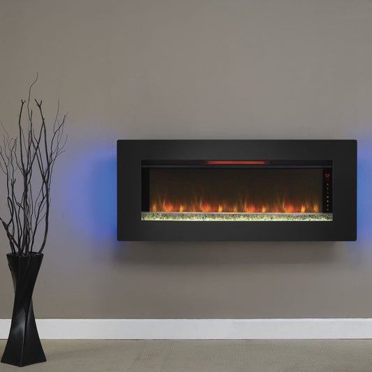 Electric fireplace mounted on a wall with a black frame, surrounded by a black chair, white lamp, and decorative plant.