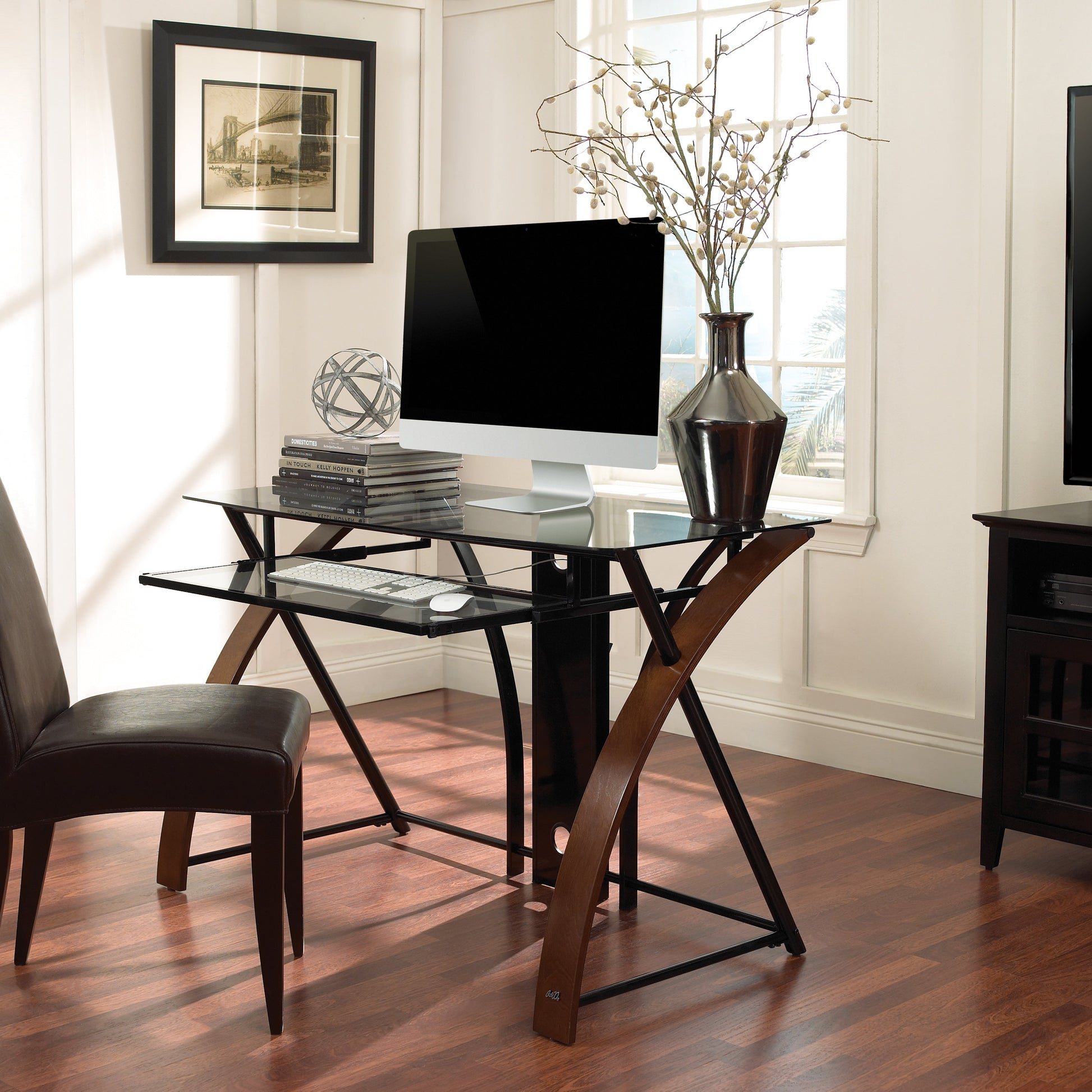 Modern home office with glass desk, chair, computer monitor, and TV.